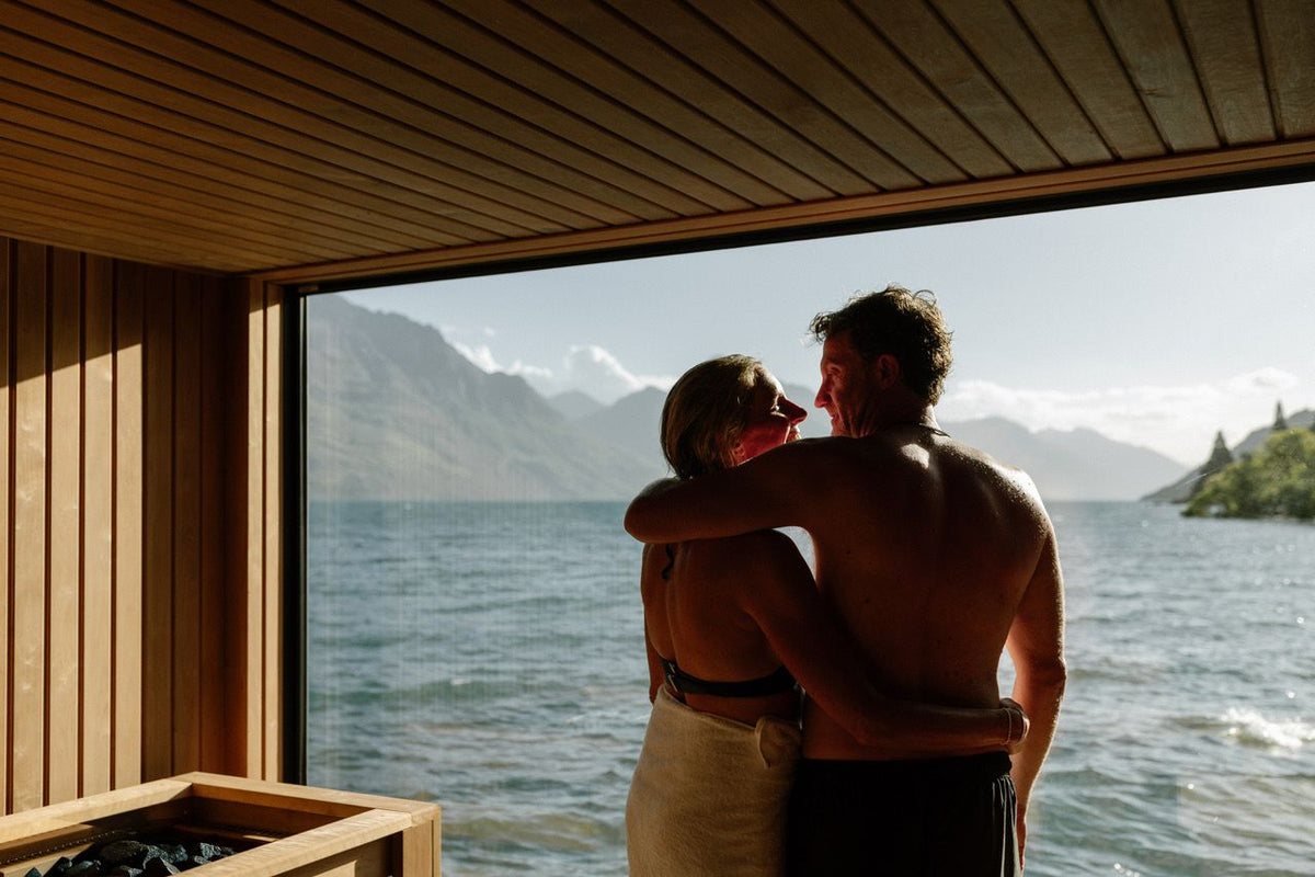 Couple embracing in sauna overlooking lake and mountains, sauna for mental health