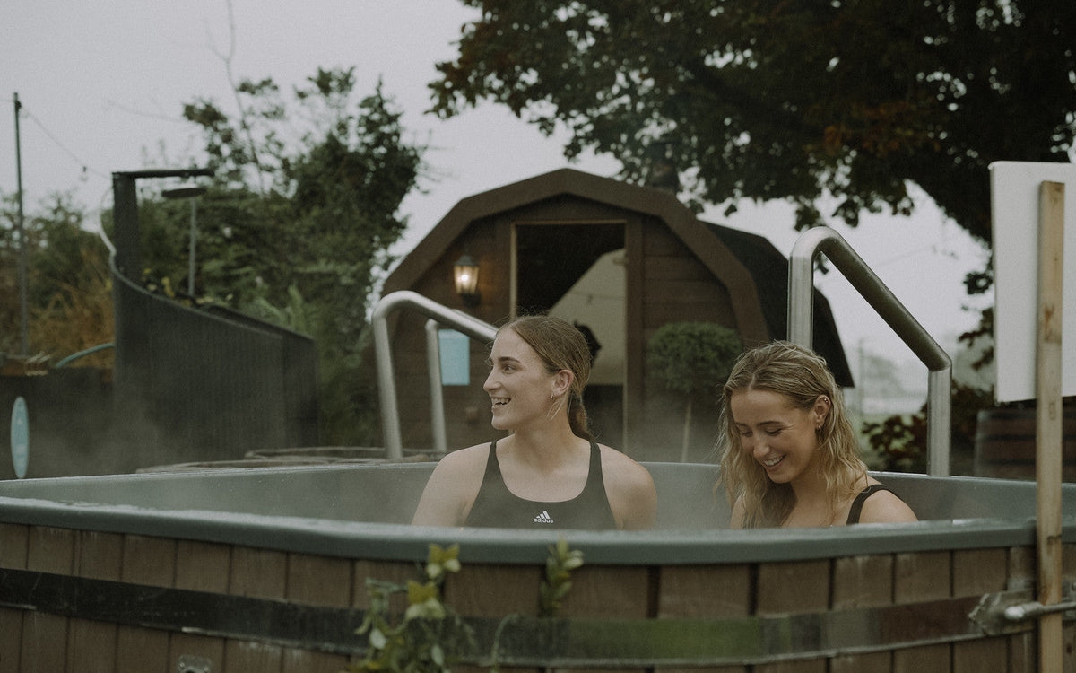Two athletes in a cold plunge tub with steam rising, cold plunge and sauna contrast therapy