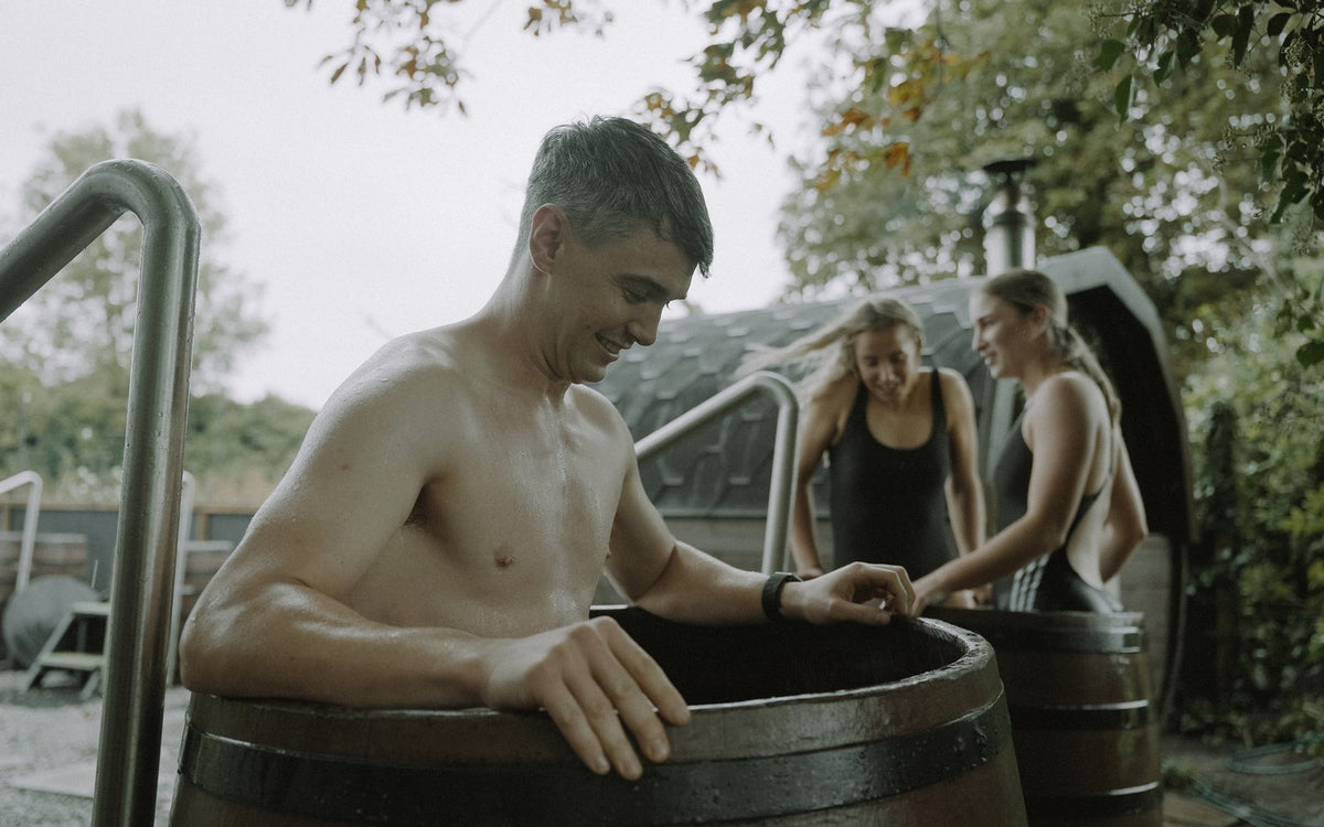 Athlete in a cold plunge barrel after a sauna session, two teammates behind at Loch Rí